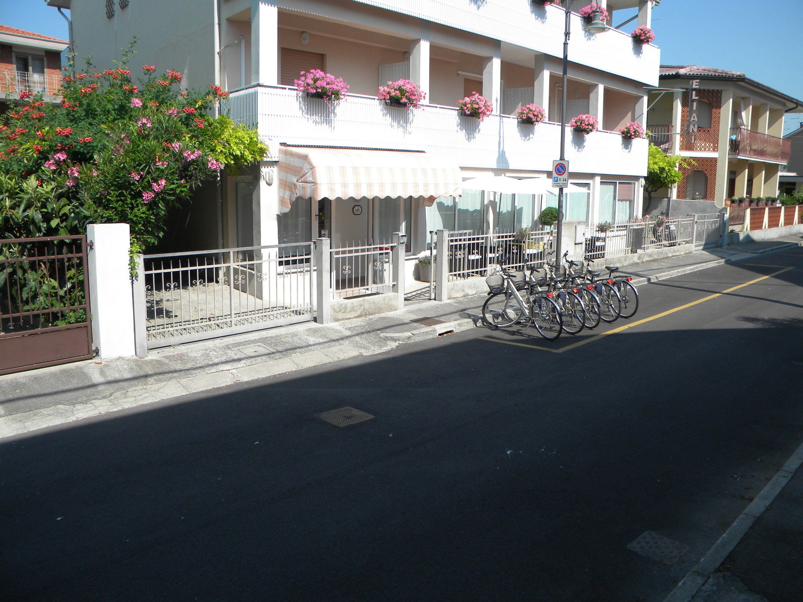 A building with a white facade, balconies with pink flowers, and bicycles parked in front.