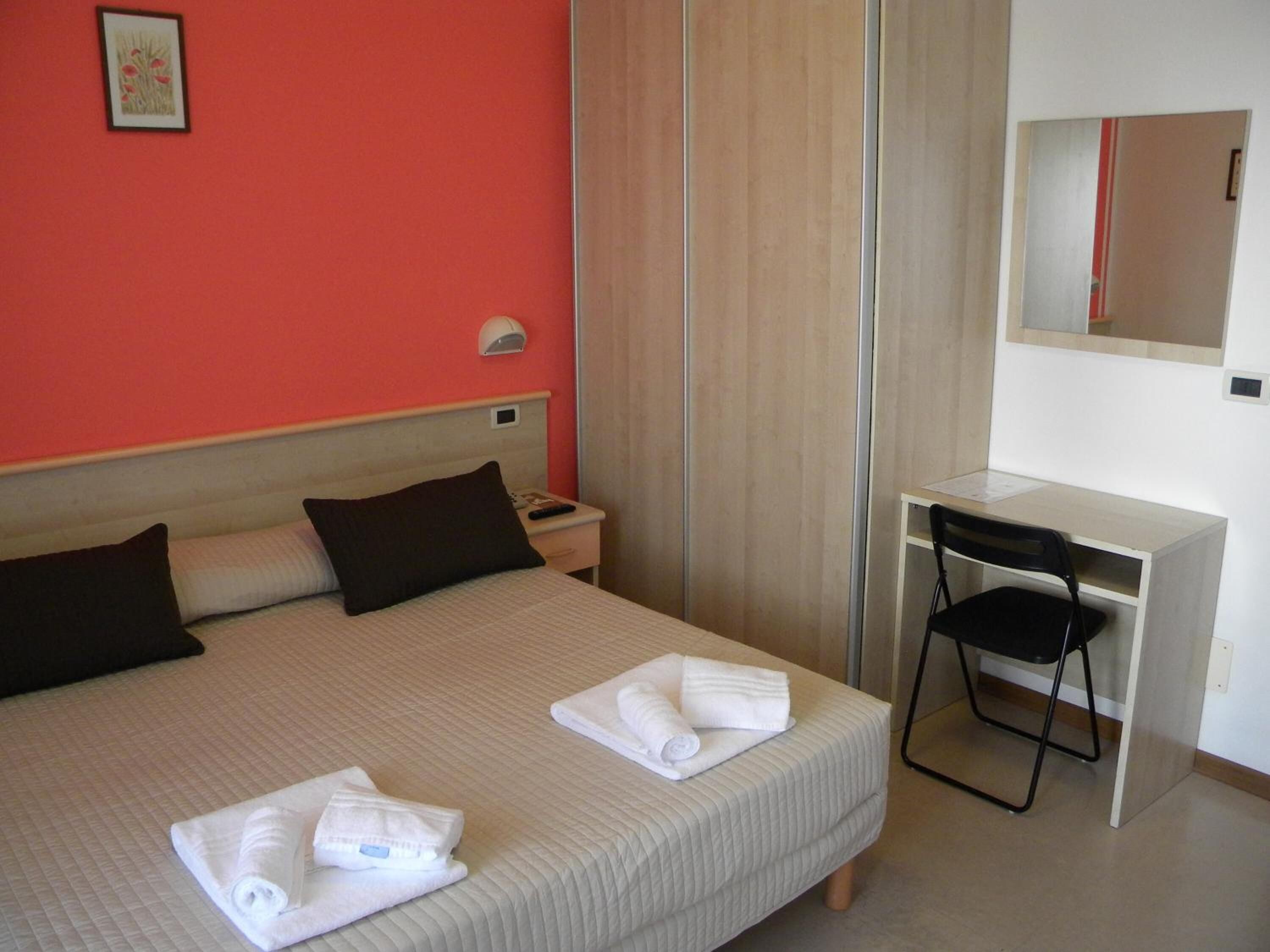 Una habitación de hotel con una cama, un escritorio, una silla y un espejo.
