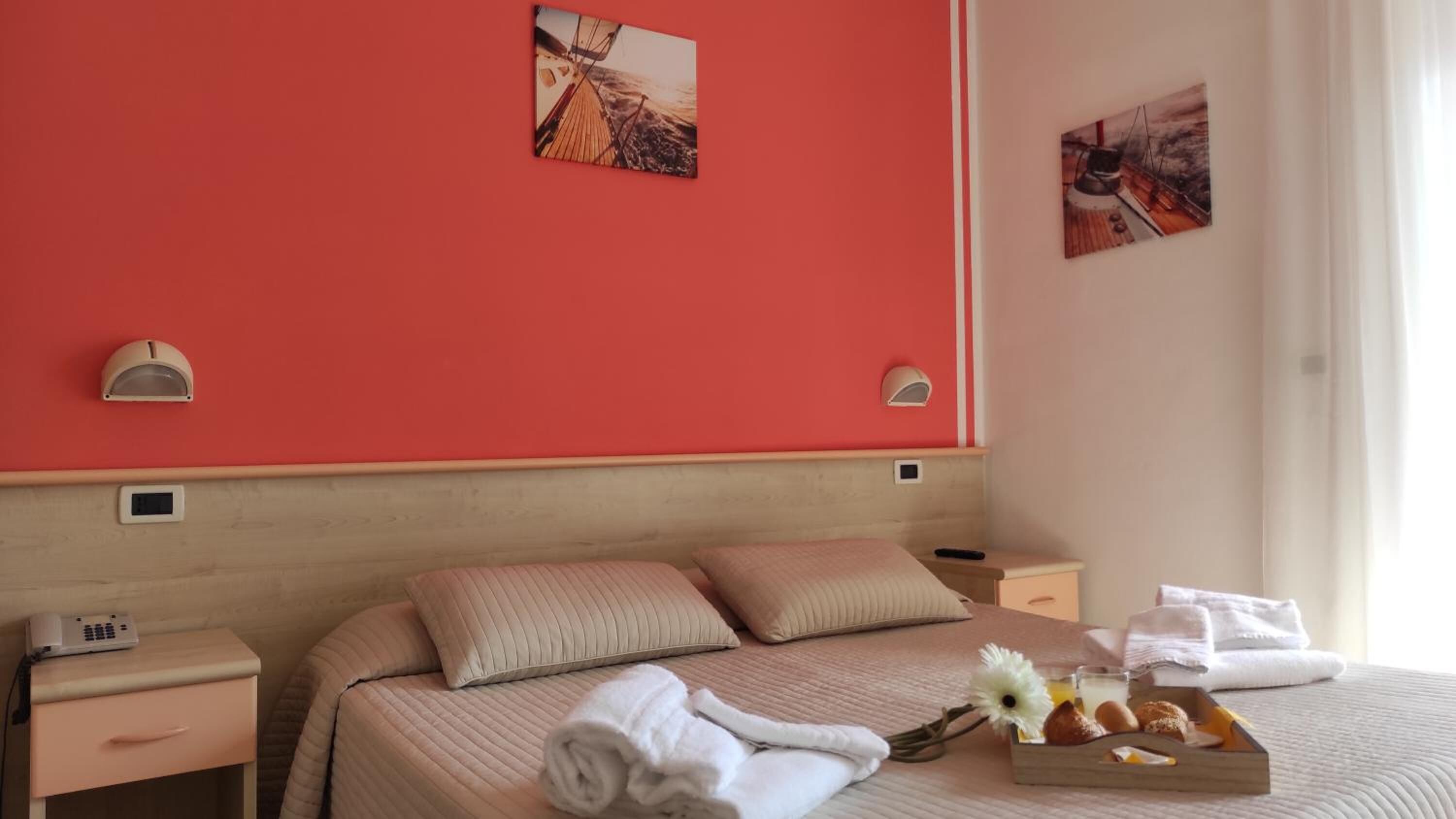 Habitació d'hotel amb un llit gran, dues taules de nit, una tauleta auxiliar, una làmpada penjada a la paret i una safata amb menjar per esmorzar.