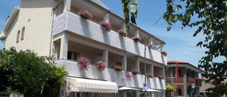 A multi-story building with balconies adorned with flowers, a white awning, and a clear blue sky.