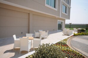 An outdoor patio area with white wicker furniture and a flower bed. - Elite Hotel Darica (Darica)