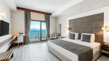 Habitación de hotel con una cama grande, un escritorio, una silla, un televisor y vista al mar.