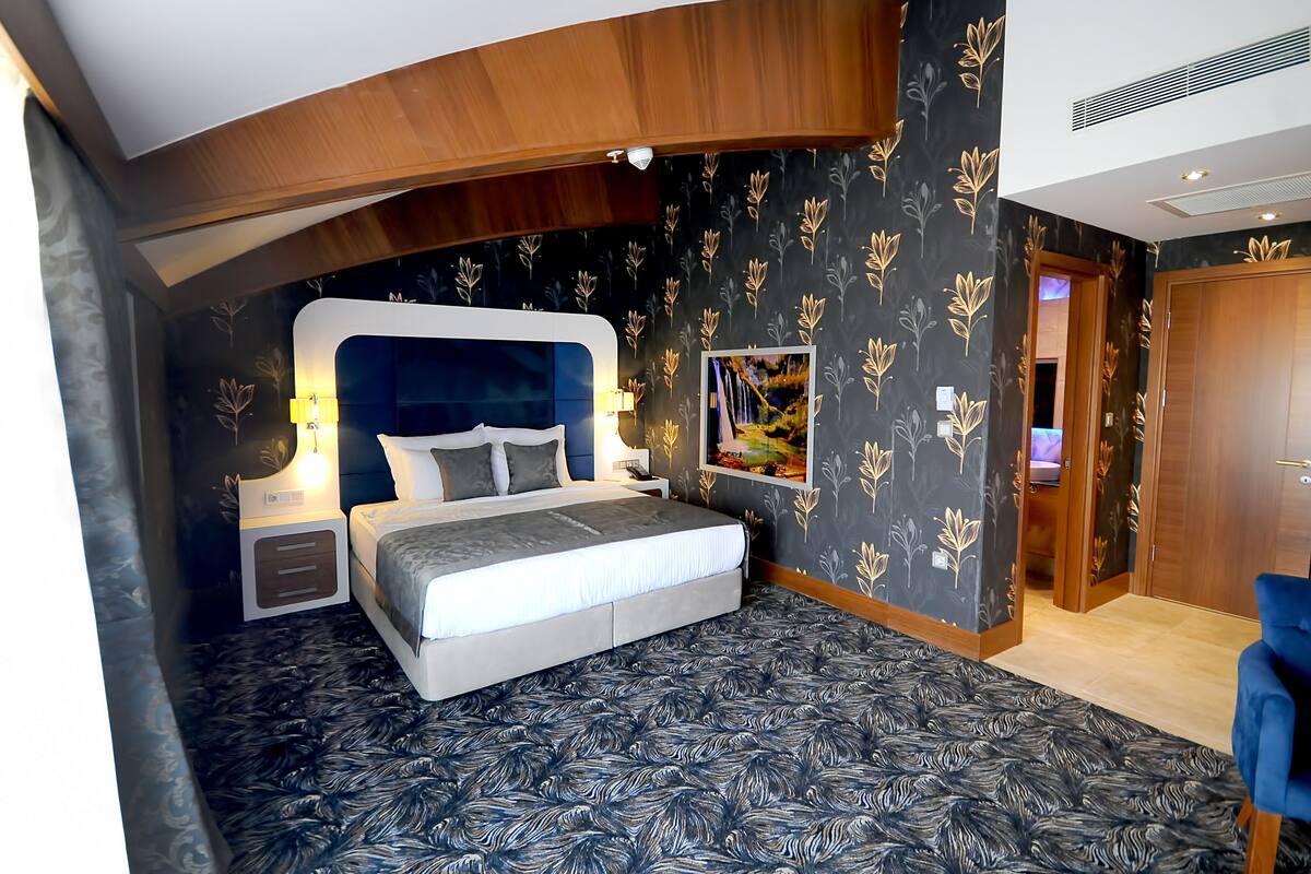 Ein Schlafzimmer mit einem Bett, Nachttischen, einem an der Wand montierten Fernseher und einer Tür zu einem anderen Raum.