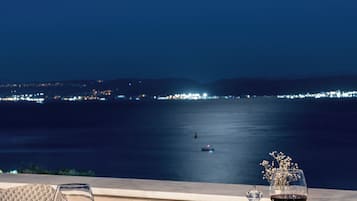 Ein Esstisch, gedeckt für ein Abendessen, mit Blick auf das Meer und eine Stadtlandschaft im Hintergrund.