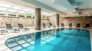 A large indoor swimming pool with multiple lounge chairs and a stone wall.