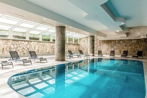 A large indoor swimming pool with multiple lounge chairs and a stone wall.