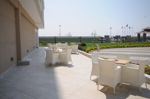 An outdoor patio with white wicker furniture and a view of a landscaped garden. - Elite Hotel Darica (Darica)