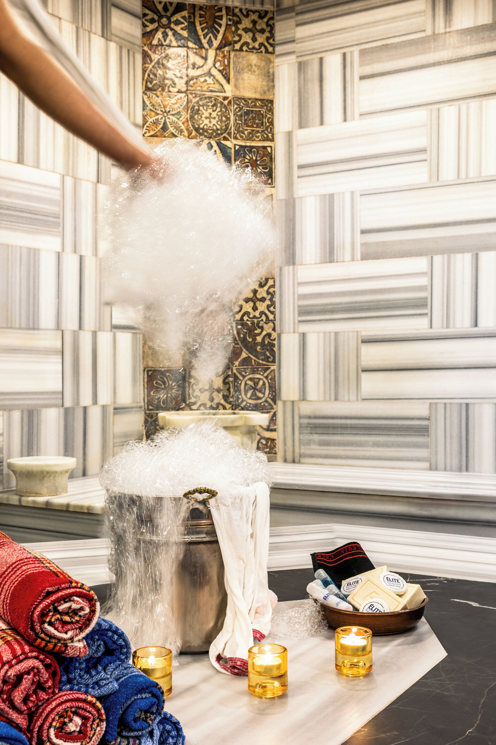 Ein Badezimmer mit einer Badewanne voller Bläschen, einem Handtuch, Kerzen und Pflegeprodukten.