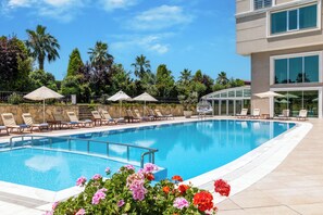 A swimming pool with lounge chairs and umbrellas, surrounded by greenery and a modern building. - Elite Hotel Darica (Darica)