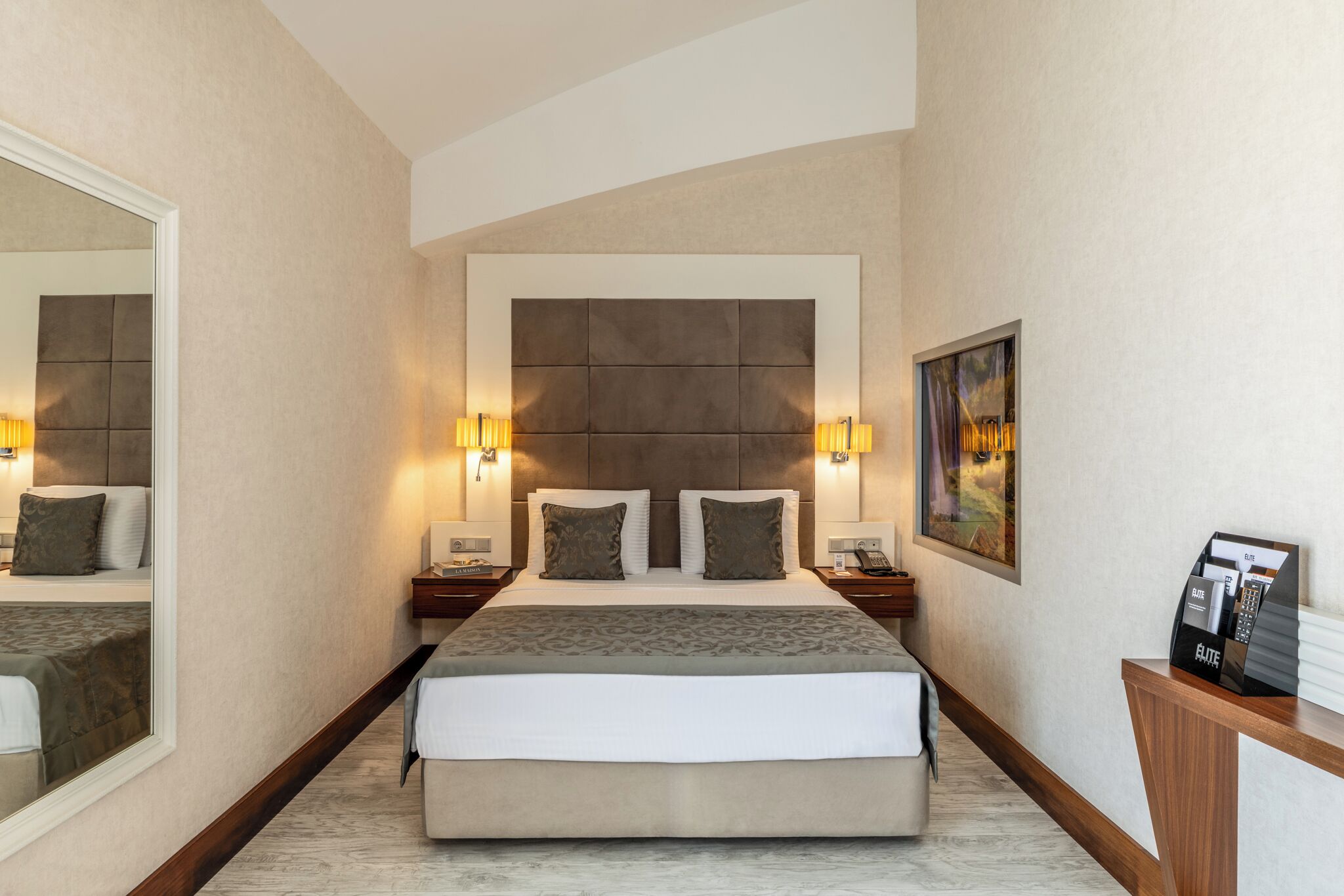 Una habitación de hotel con una cama grande, lámparas de noche, un espejo, un cuadro y un minibar.