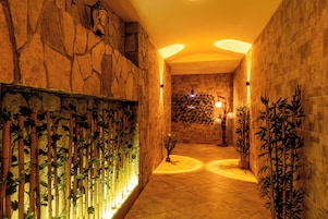 A corridor with stone walls, bamboo plants, and a Buddha statue.