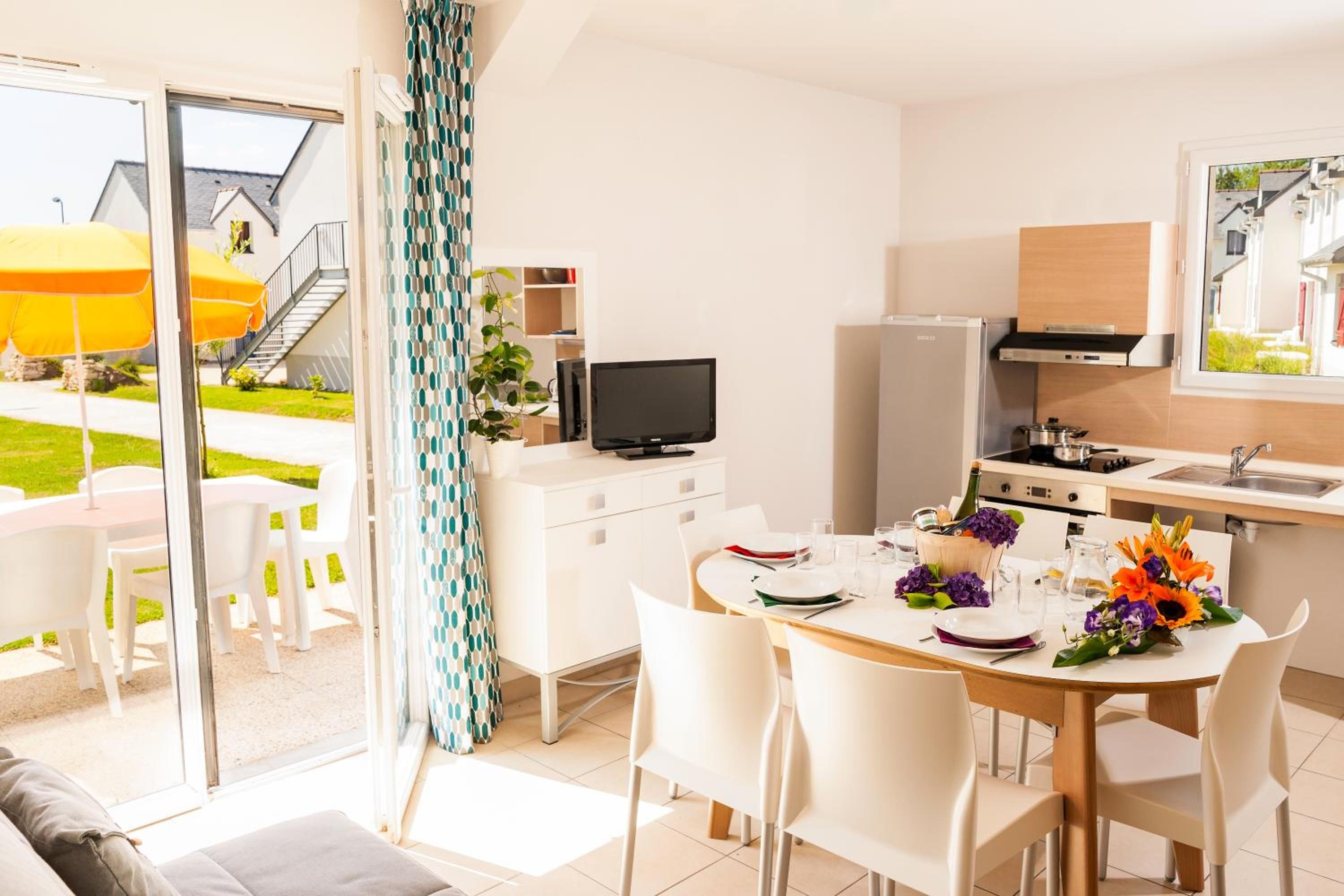 A modern kitchen with a dining area, a TV, and a view of a house and garden.