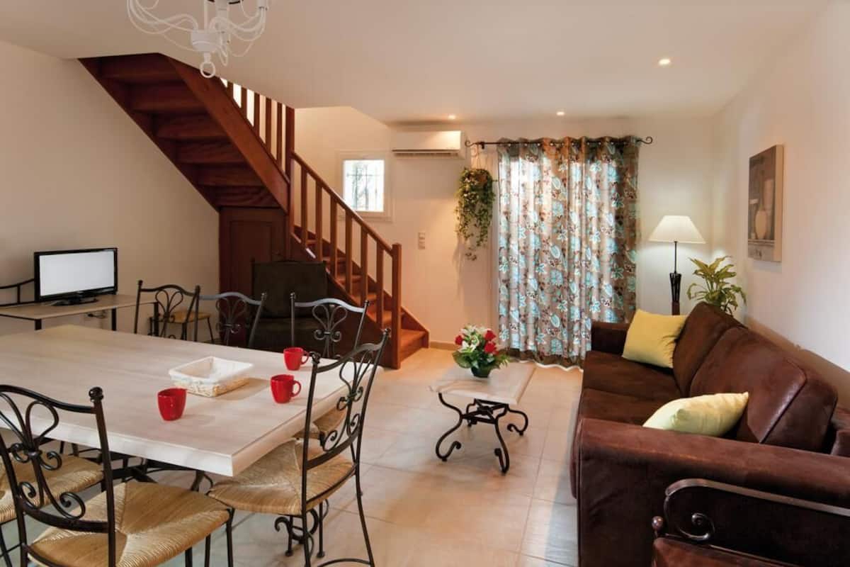 A dining area with a wooden staircase, a dining table with chairs, a sofa, and a lamp.