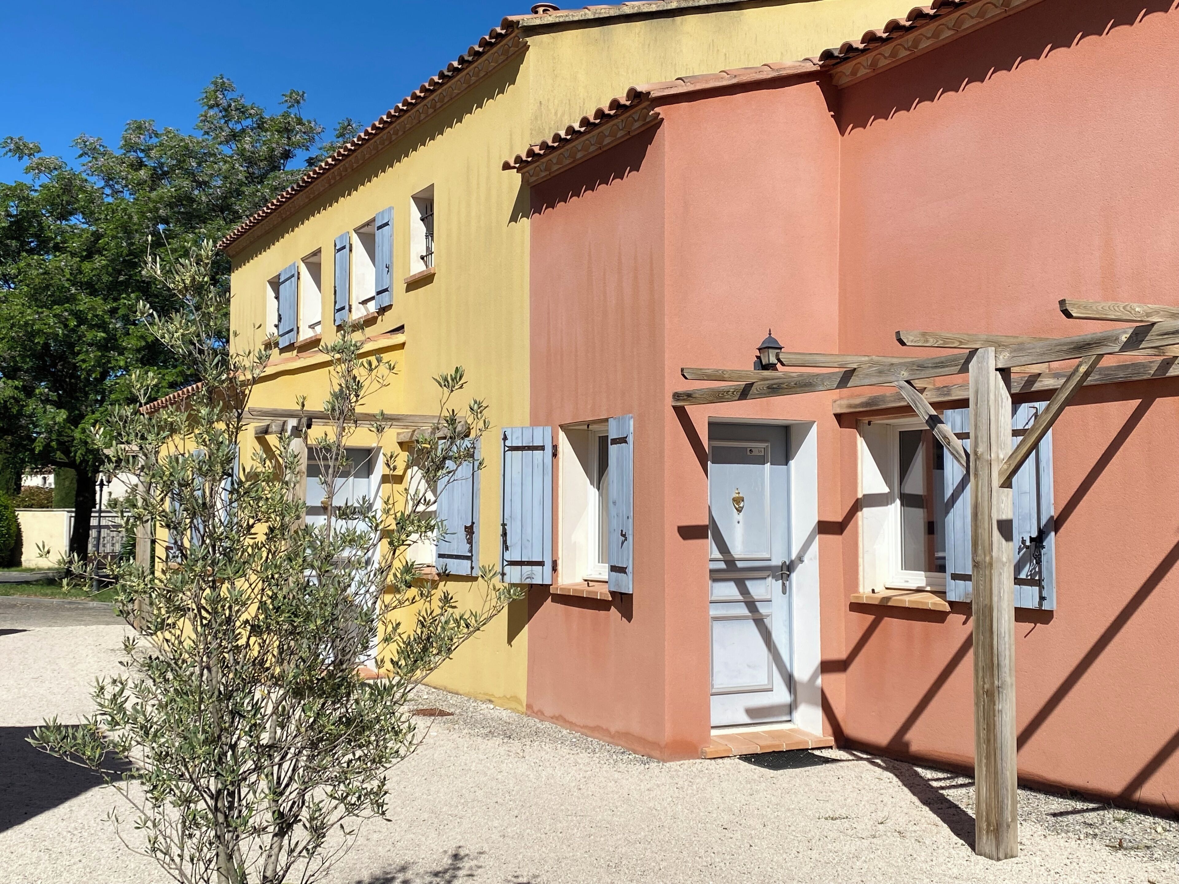 A building with a yellow facade, a red section, and a wooden pergola with a lantern.