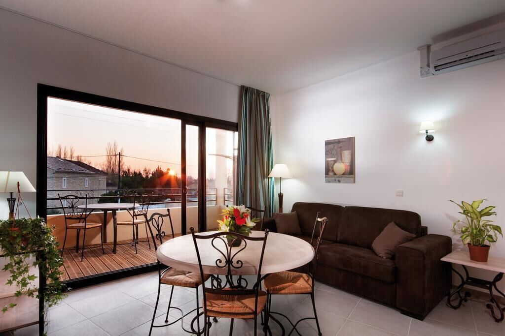 Una sala de estar moderna con balcón, un sofá marrón, una mesa de comedor con sillas y una planta en maceta.