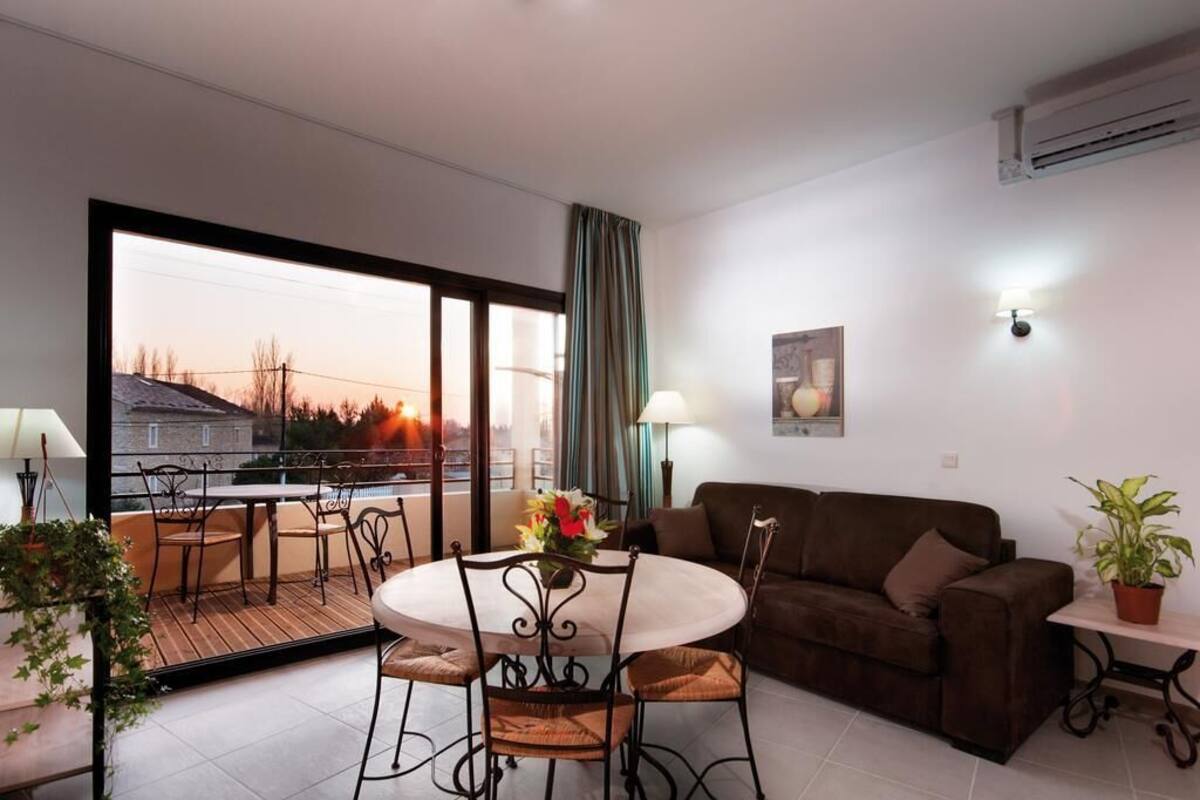 Ein modernes Wohnzimmer mit Balkon, einem braunen Sofa, einem Esstisch mit Stühlen und einer Topfpflanze.