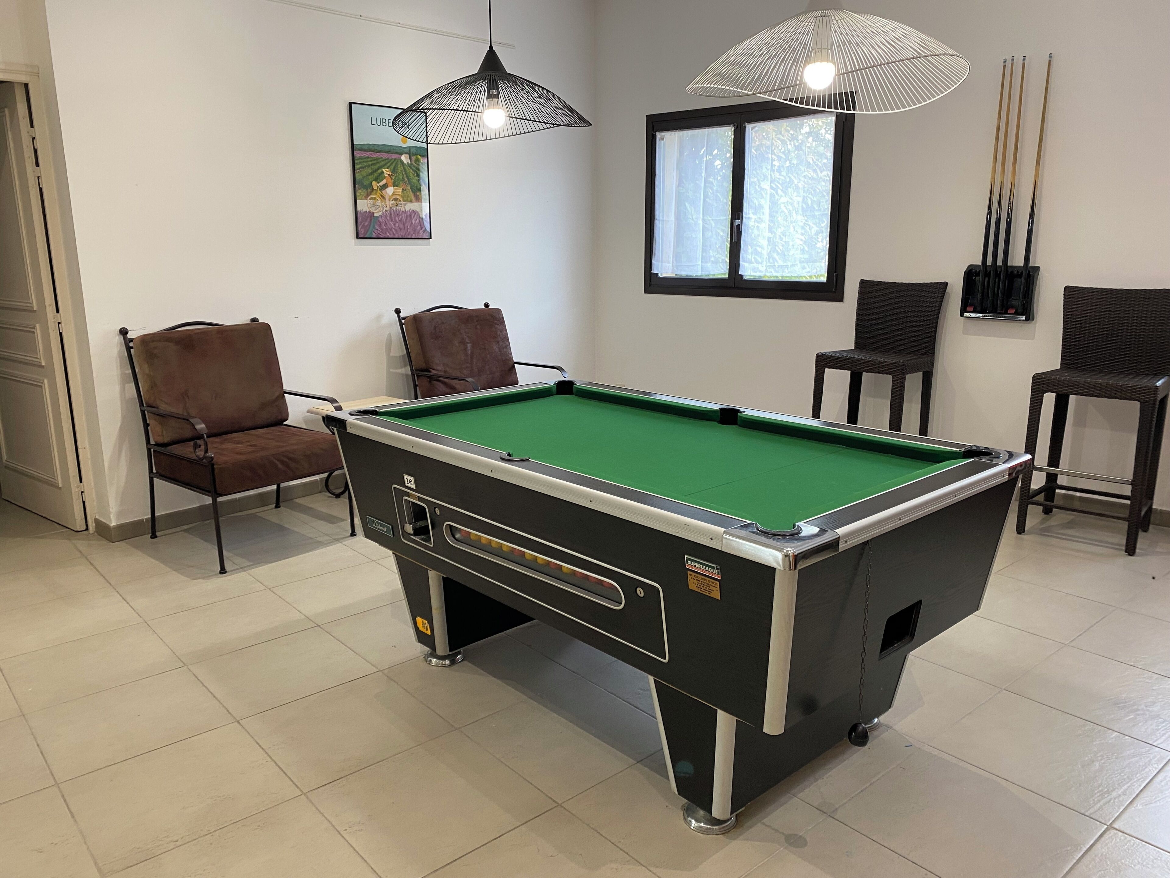 A pool table in a room with chairs, a window, and a wall-mounted lamp.