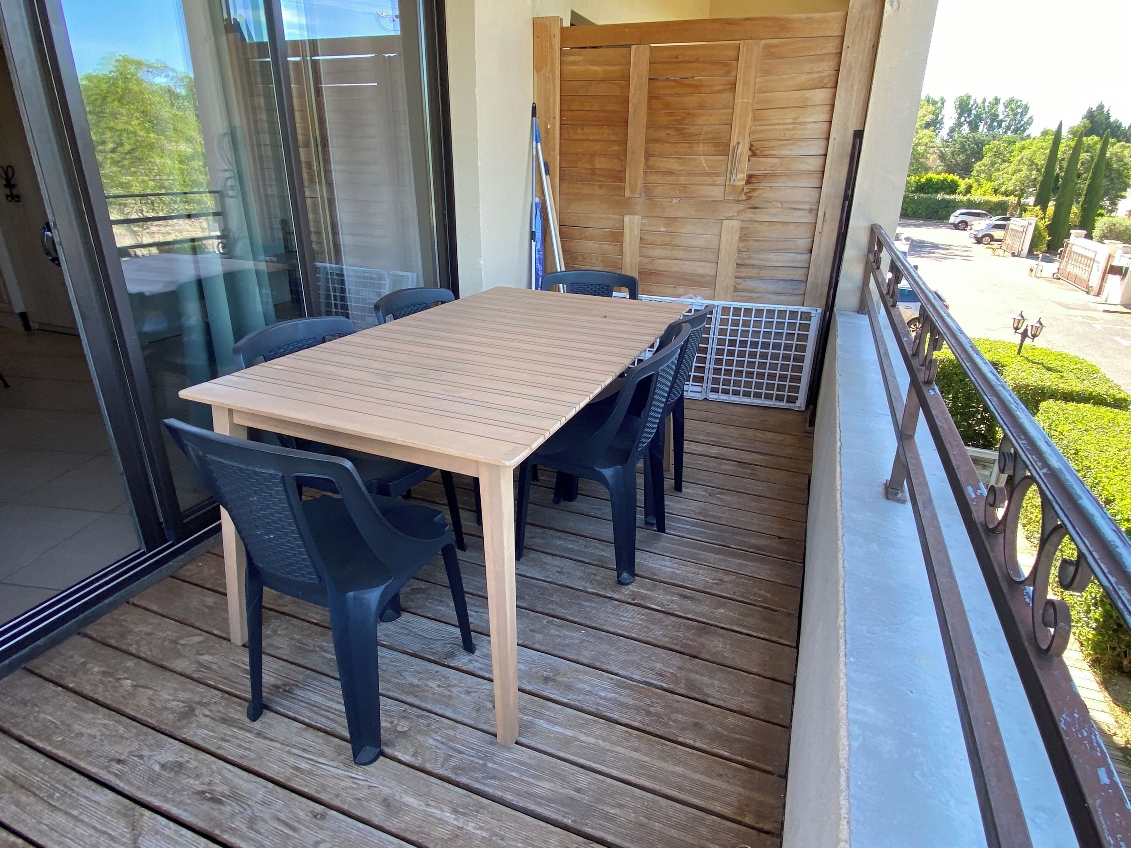 A balcony with a wooden table and chairs, a glass door, and a view of the street.