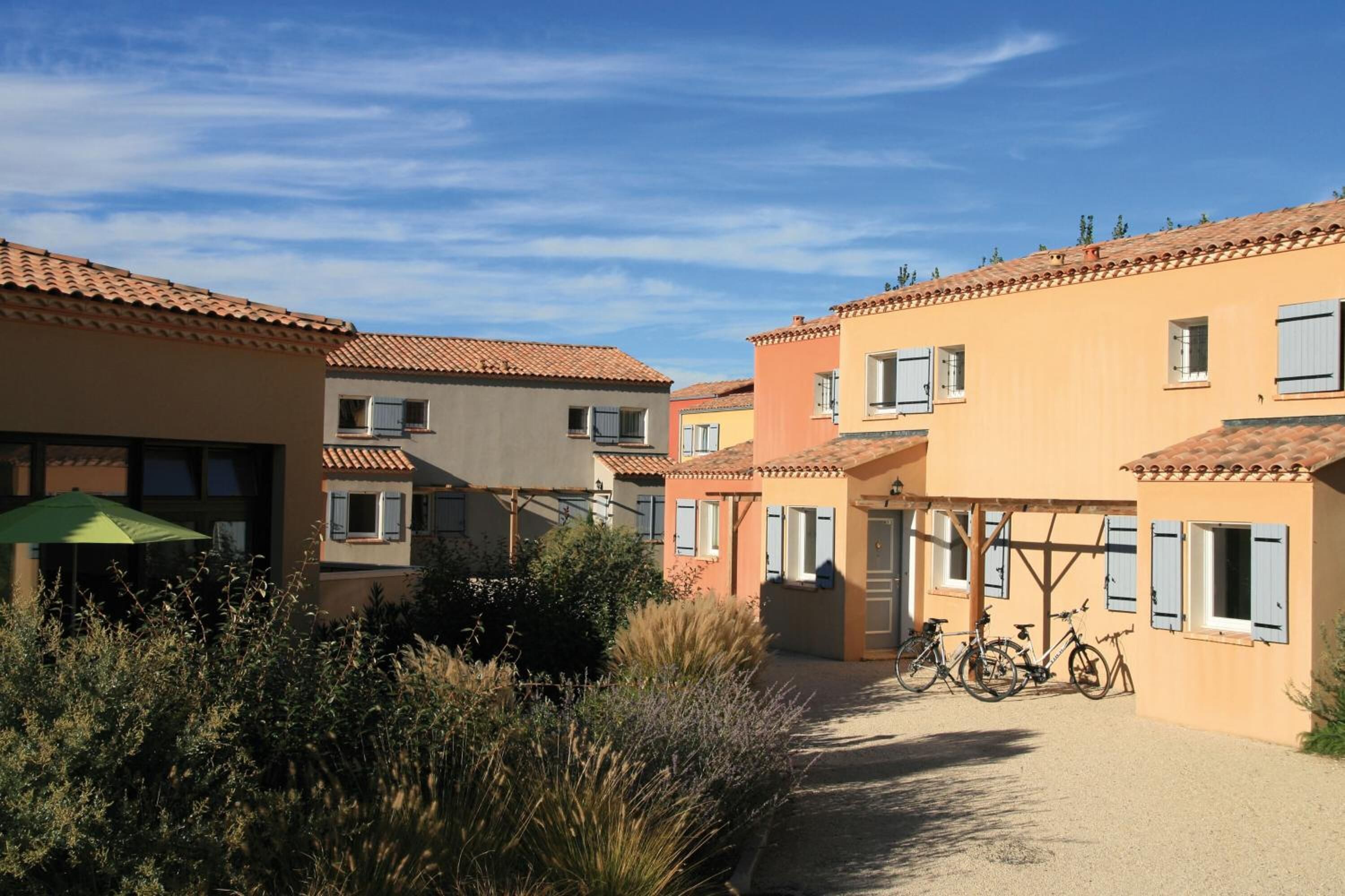 Une rangée de bâtiments aux toits de tuiles rouges, dotés de balcons, avec des vélos garés devant et un chemin de gravier.