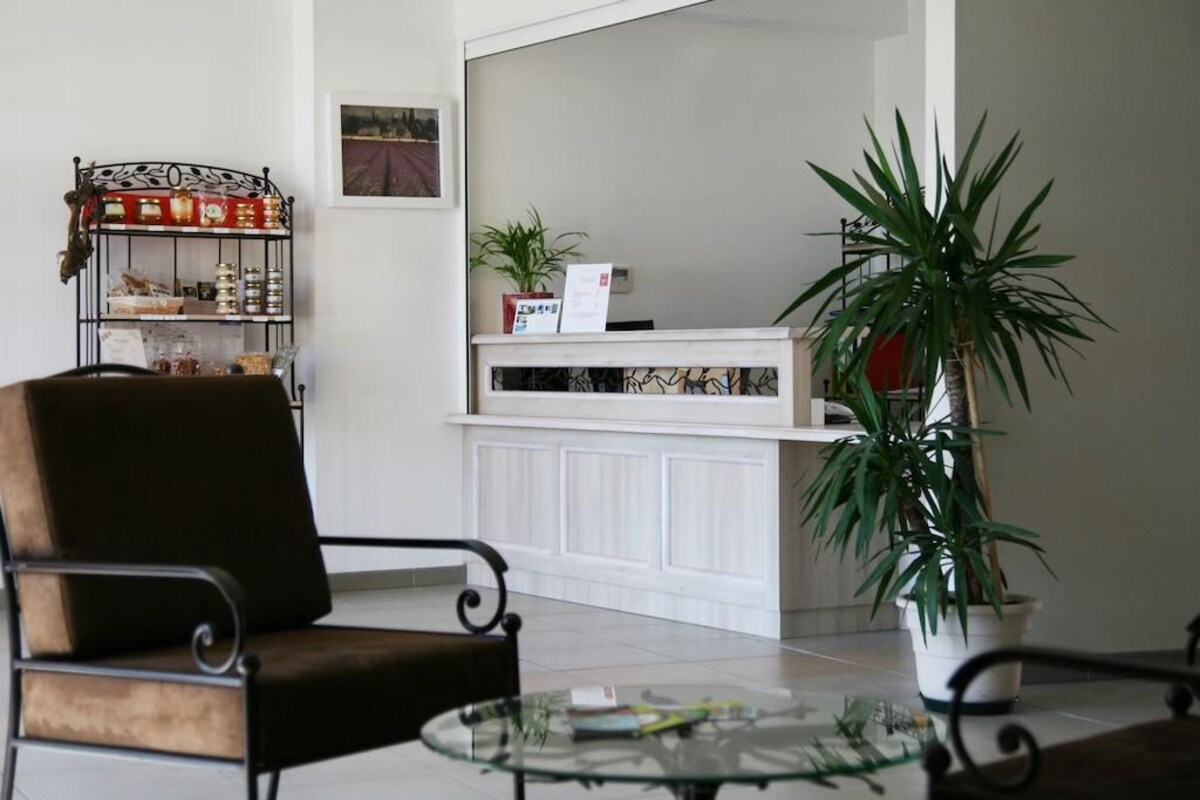 A reception area with a white counter, a chair, a glass table, and a potted plant.