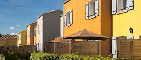 A row of yellow buildings with white shutters, wooden fences, and green hedges.