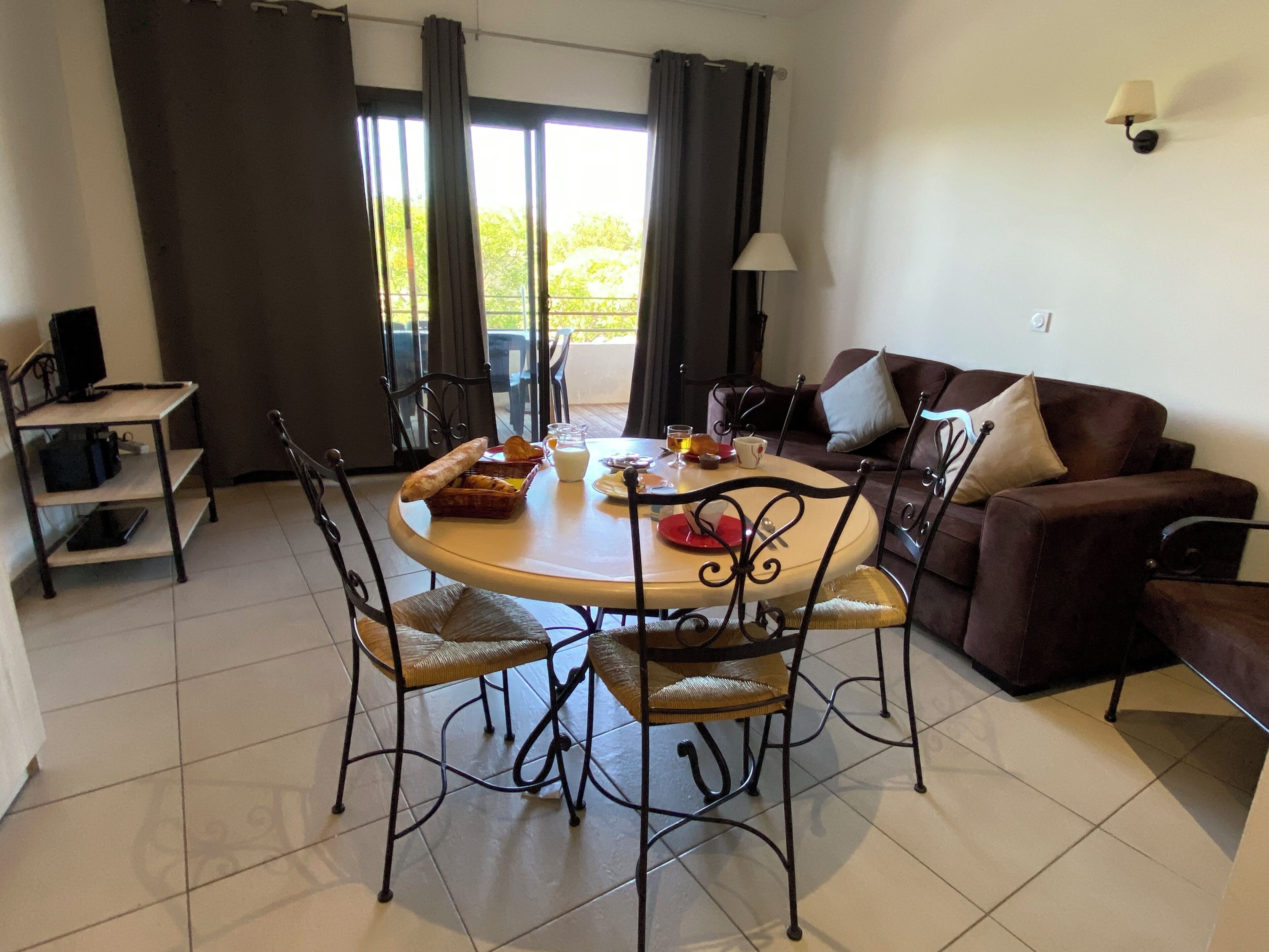 Un comedor con una mesa redonda, sillas, un sofá y un televisor sobre una estantería.