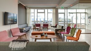 A modern waiting area with comfortable seating, a flat-screen TV, and large windows offering a view of the outside. - Geo Hotel Grindavik (Grindavik)
