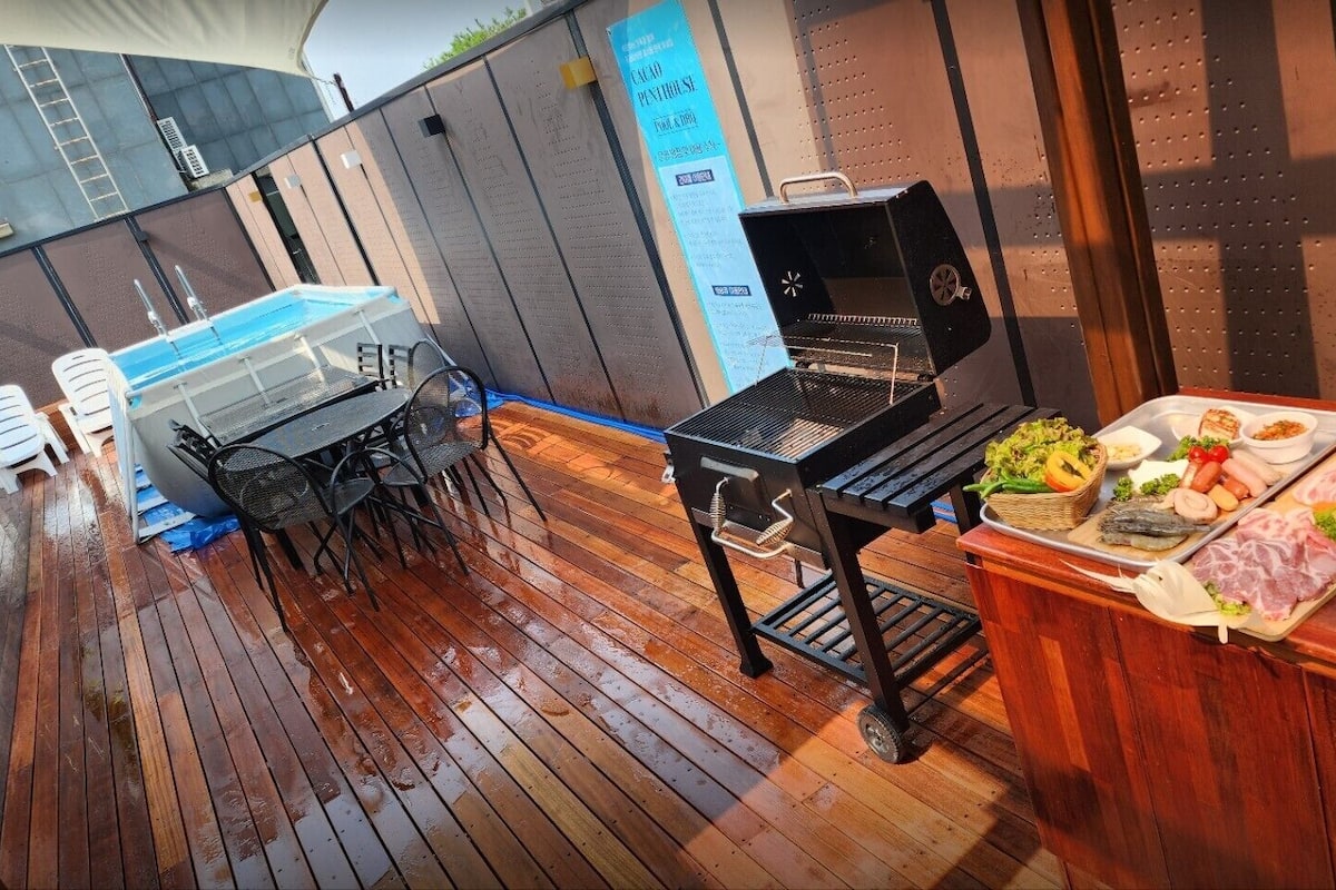 Een houten terras met een barbecue en een tafel vol eten.