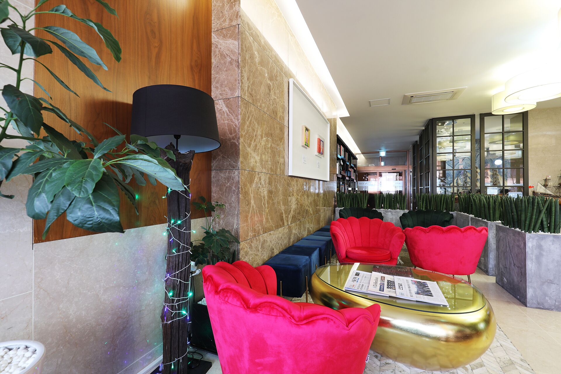 A modern lounge area with a wooden accent wall, a tall floor lamp, and a seating arrangement with red and blue chairs.