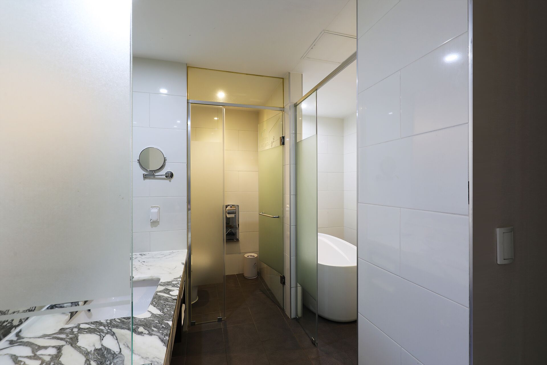 A modern bathroom with a glass shower enclosure, a white sink, and a marble countertop.