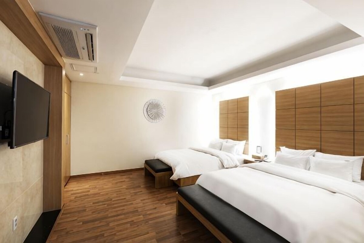A modern hotel room with a large bed, a bench, a TV, and a wooden headboard.