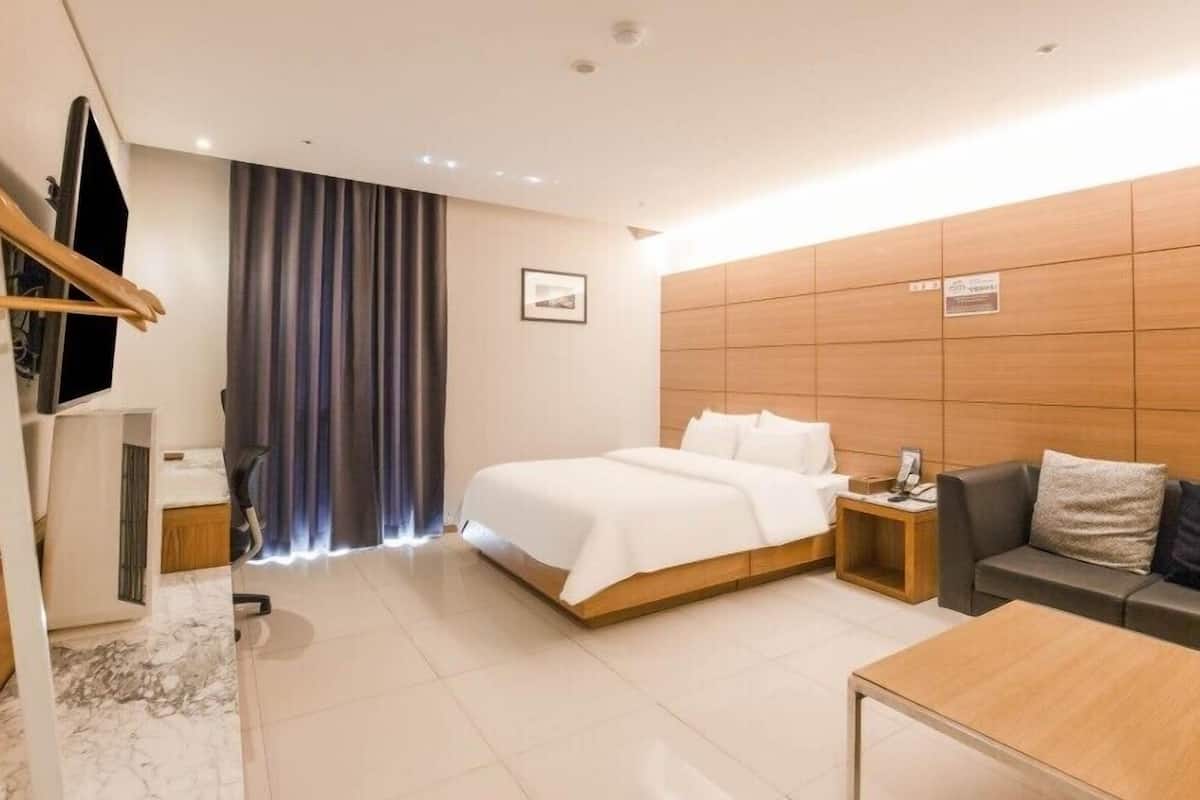 Een hotelkamer met een bed, een bank, een salontafel, een televisie en een gordijn.