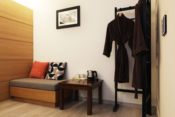 Una habitación compacta con sofá, una mesita con hervidor y perchero.
