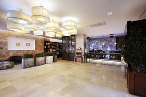 Vestíbulo de hotel con una recepción, estanterías y suelo de mármol.
