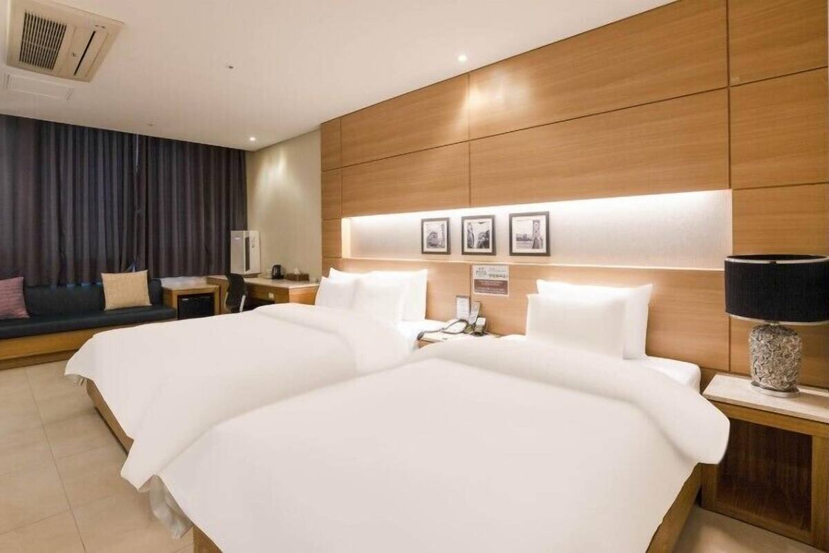 Een hotelkamer met twee bedden, een sofa, een bureau en een lamp.