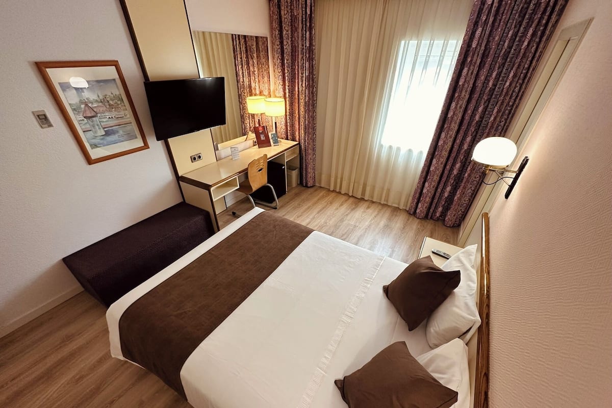 A hotel room with a bed, a desk, a chair, a TV, and curtains.