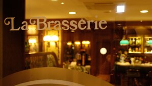 Interior borroso de un restaurante con el nombre 'La Brasserie' visible en el ventanal.