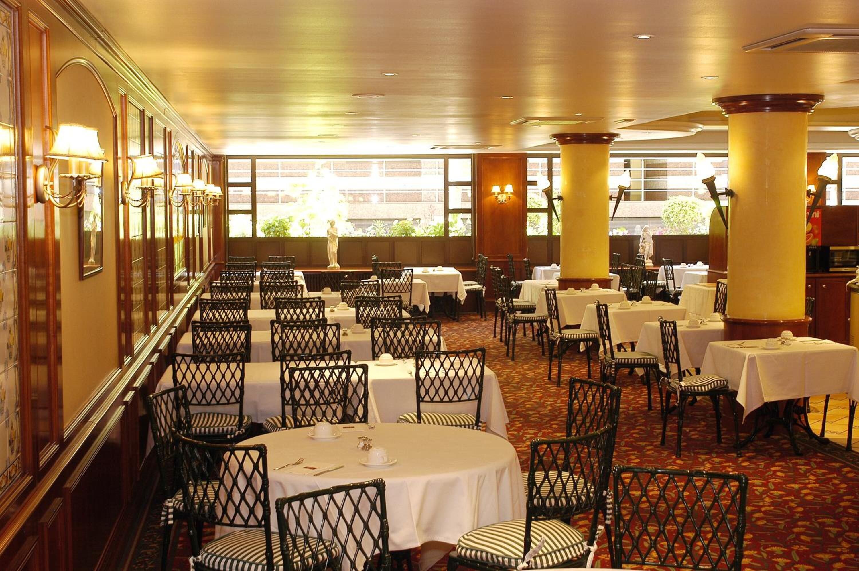 Un restaurante con mesas redondas, sillas de mimbre negro y manteles blancos.