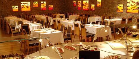 A restaurant with multiple tables, each set with white tablecloths and chairs, and a variety of dishes on the tables.