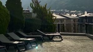 Una terraza con sillones de descanso, un muro de piedra y vistas a montañas lejanas y un pueblo.