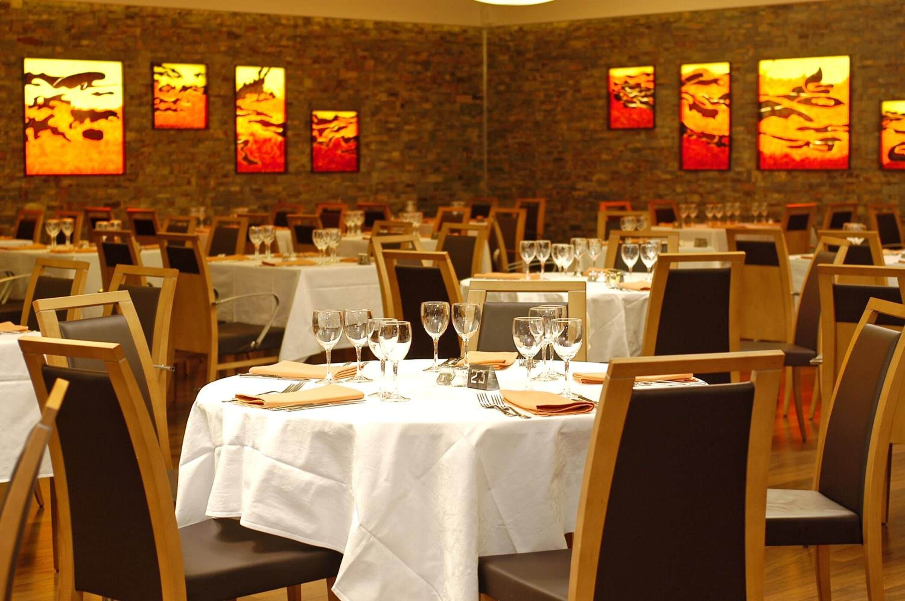 A restaurant with multiple tables set for dining, each with a white tablecloth and chairs.