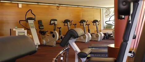 Un gimnasio con diversos equipos de ejercicio, incluyendo cintas de correr y bicicletas estáticas, dispuestos en filas.