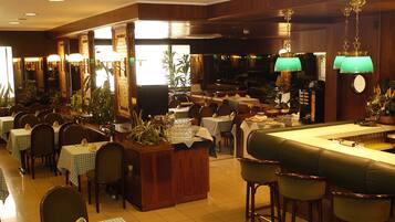 Un restaurant doté de nombreuses tables et de banquettes, d’une décoration en bois et de lampes vertes suspendues.