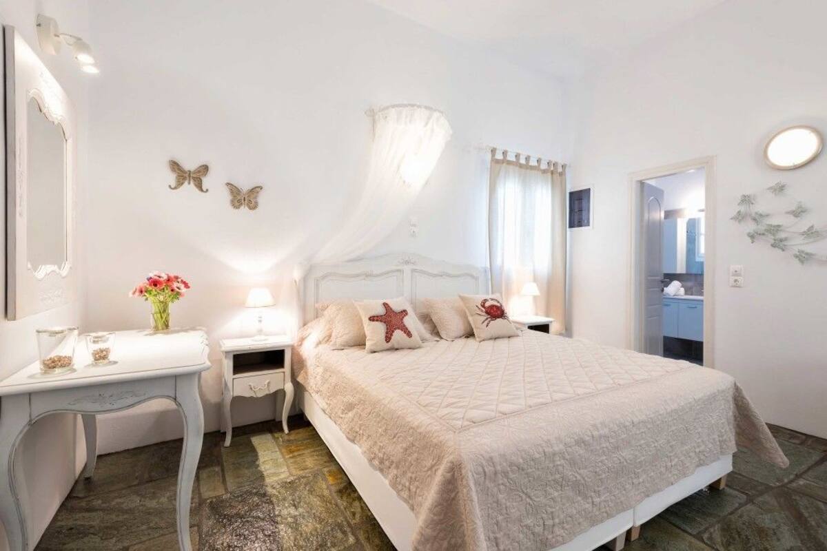 Quarto com cama, mesas de cabeceira, penteadeira, espelho e janela com cortinas.