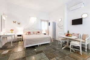 A bedroom with a bed, bedside tables, a desk, a chair, a sofa, a TV, and a fruit bowl. - Ambelas Mare (Paros)