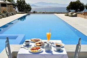 Desayuno junto a la piscina con una mesa, sillas y vista al mar.