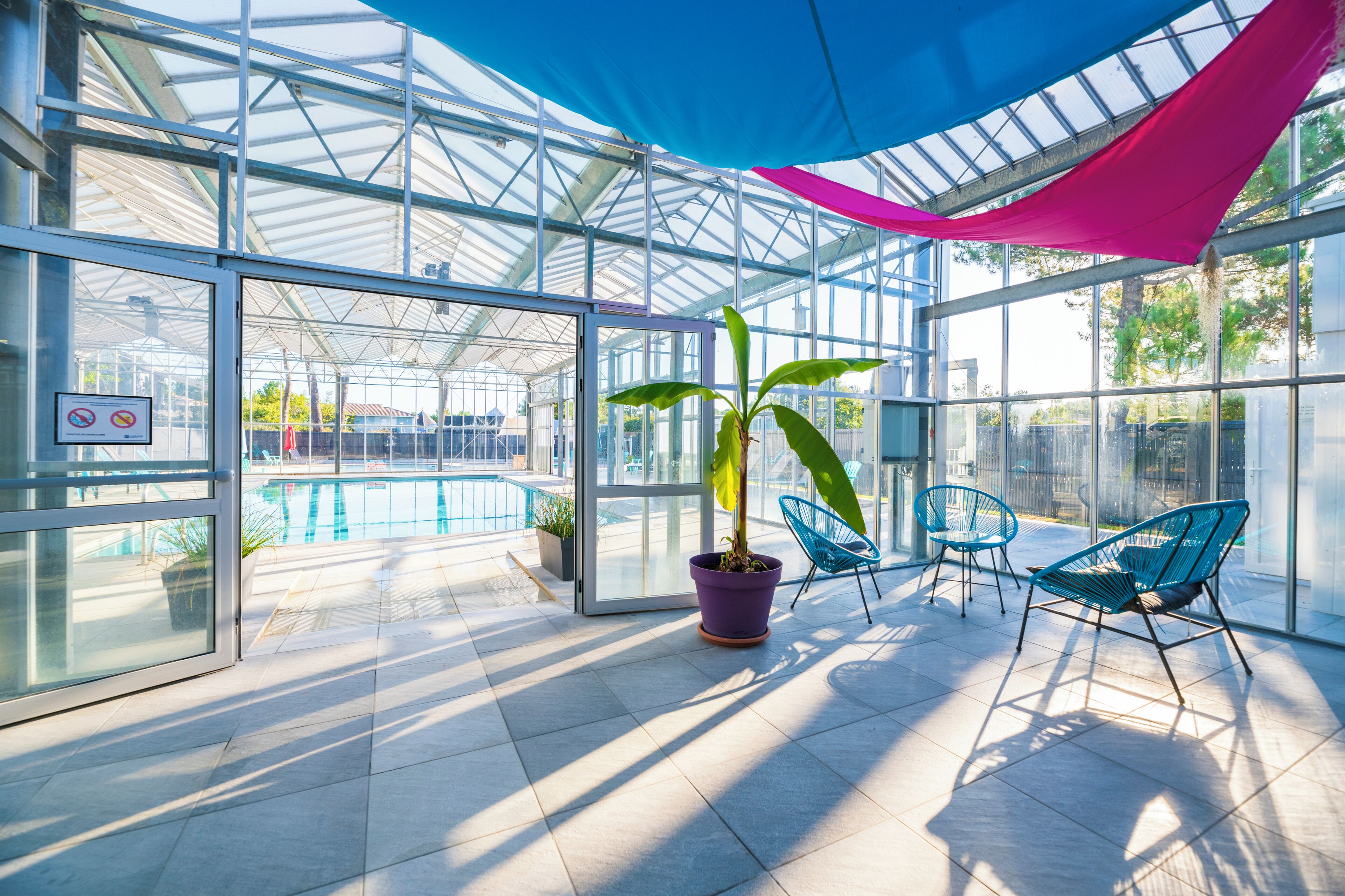 A glass-enclosed area with a pool, potted plants, and blue chairs.