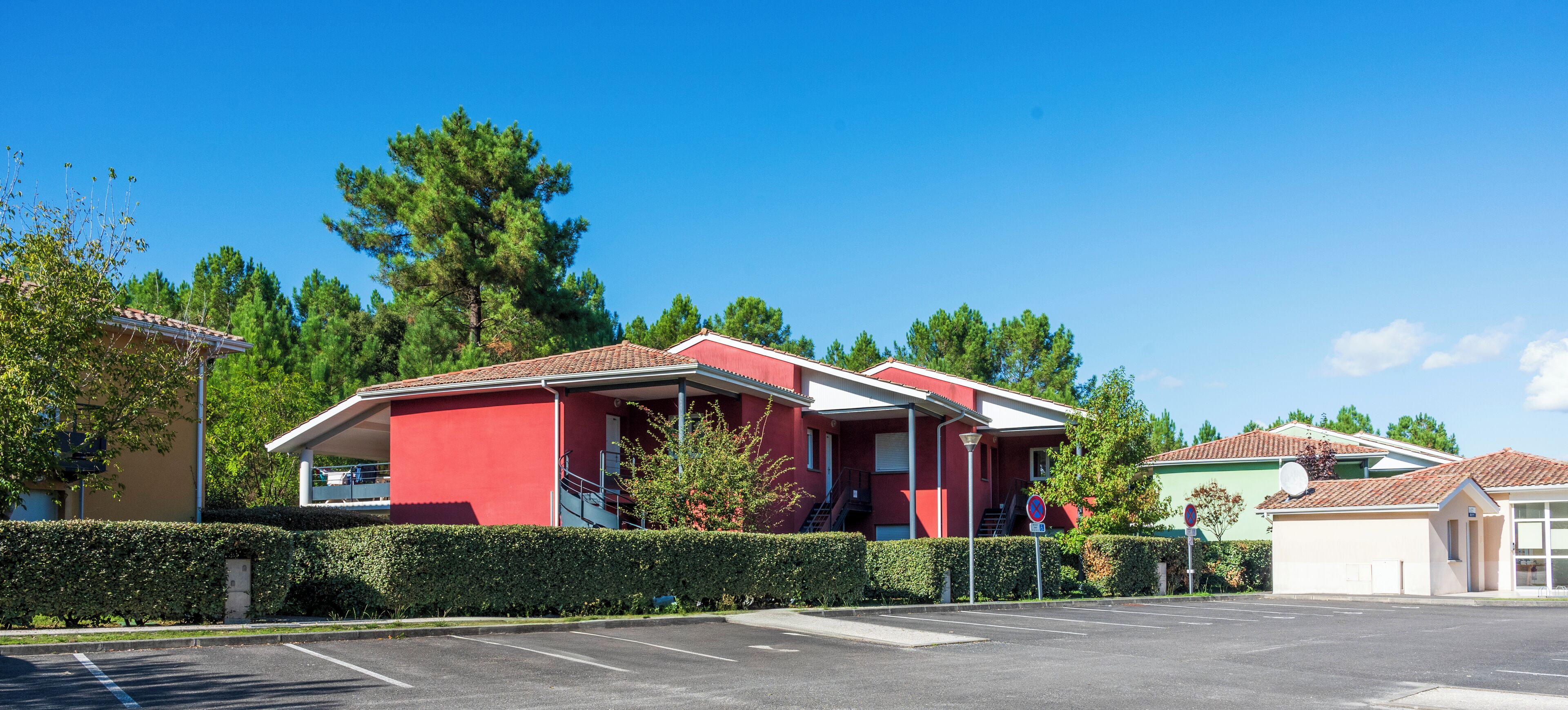 Un bâtiment rouge avec une entrée abritée et un parking situé devant.