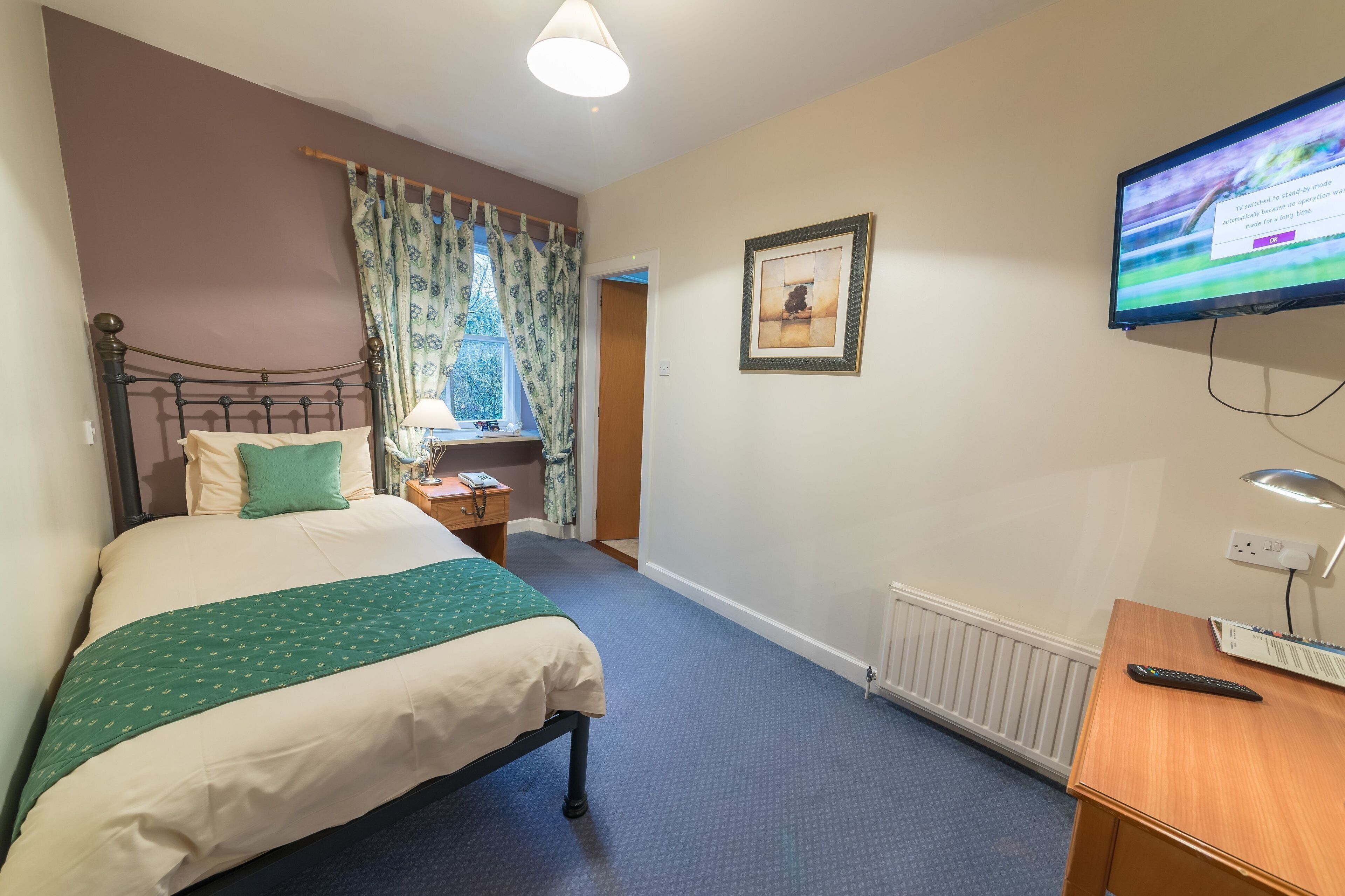 A hotel room with a bed, a desk, a television, and a window with curtains.