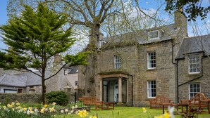 A stone building with a garden in front, including a bench and chairs.
